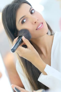 Brunette woman using powder brush in front of mirror