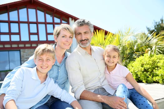 Happy family of four sitting in front of contemporary house