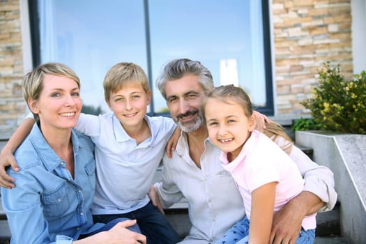 Happy family of four sitting in front of contemporary house