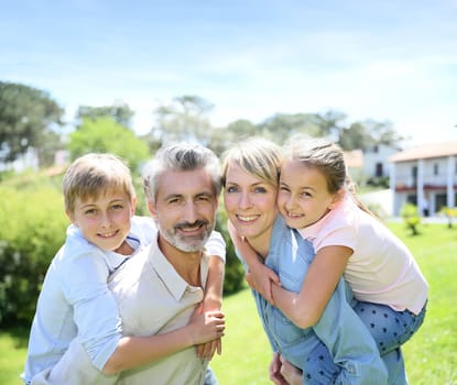 Parents giving piggyback ride to kids in garden
