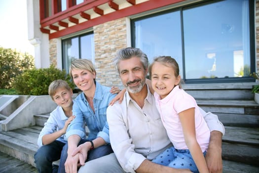 Happy family of four sitting in front of contemporary house