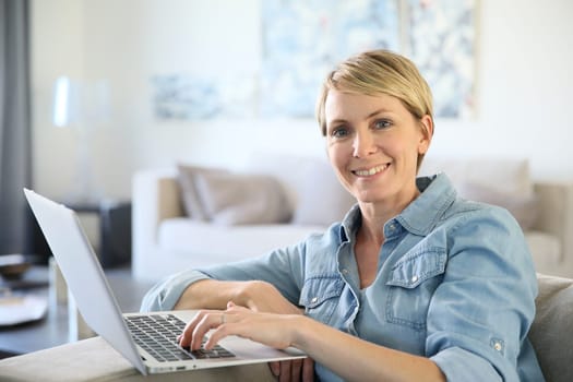 Middle-aged woman sitting in sofa and using laptop