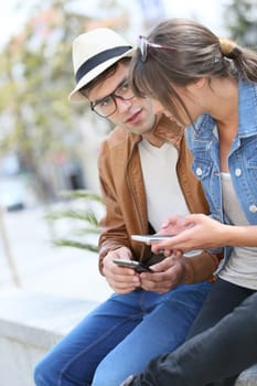 Young trendy couple in town using smartphones