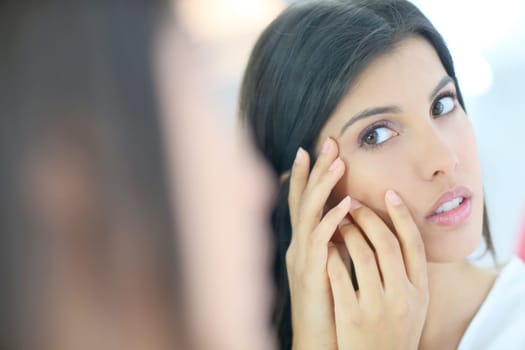 Beautiful brunette girl looking at skin in mirror