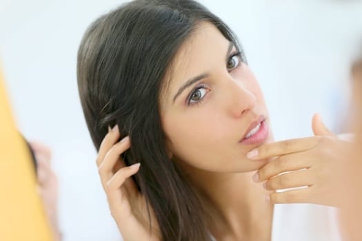 Portrait of beautiful young woman looking at her skin