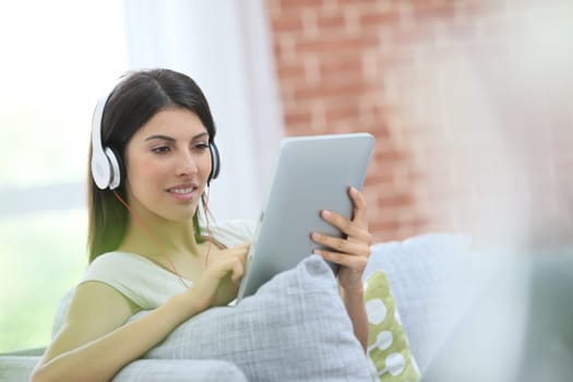Young woman with tablet and headphones sitting in sofa