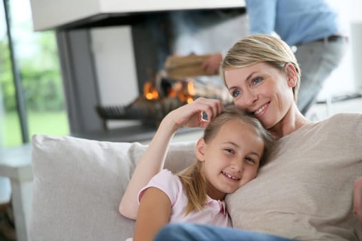 Mother and daughter relaxing by fireplace, laying in couch