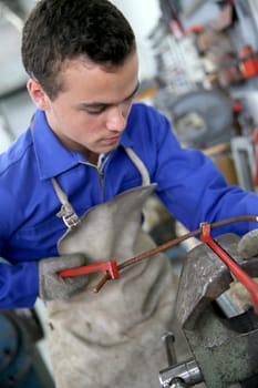 Young man in ironworks training working on steel