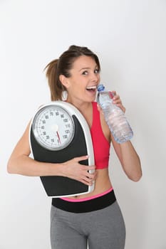 Cheerful fitness girl with bottle of water, holding scale, isolated