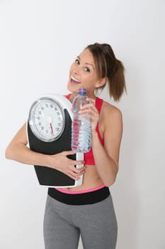 Cheerful fitness girl with bottle of water, holding scale, isolated