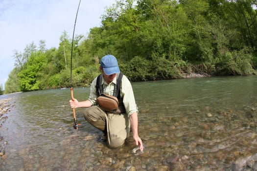 Fisherman catching brown trout with fishing line in river