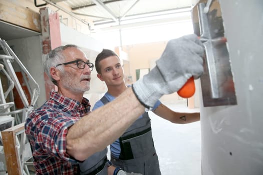 Young apprentice with professional plasterer