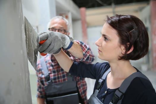 Young apprentice with professional plasterer