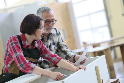 Young woman with senior craftsman in carpentry class