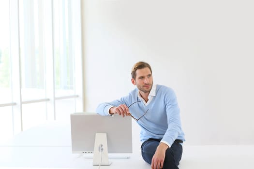Businessman sitting on table by computer in modern room