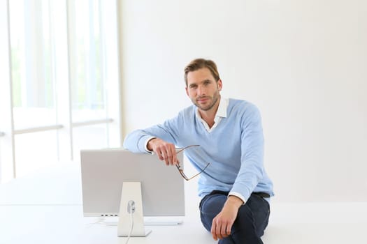Businessman sitting on table by computer in modern room