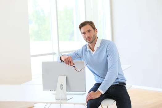Businessman sitting on table by computer in modern room