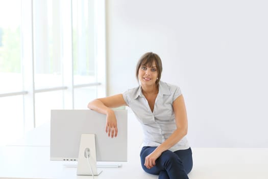 Smiling young woman sitting on table by computer