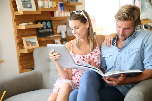 Trendy couple in coffee shop reading magazine sitting in sofa