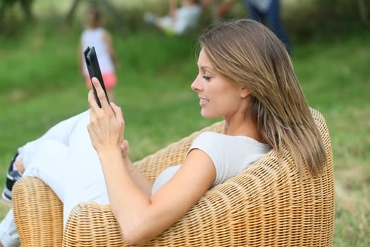 Woman relaxing in outdoor armchair and using digital tablet