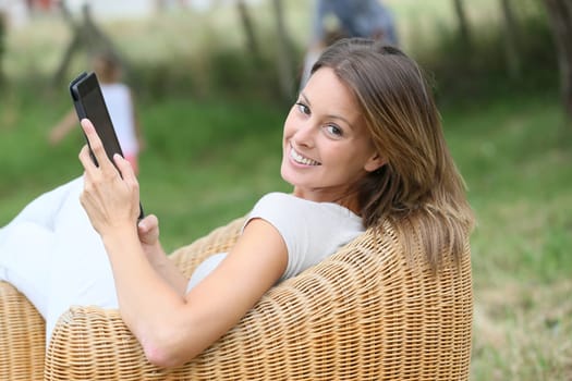 Woman relaxing in outdoor armchair and using digital tablet