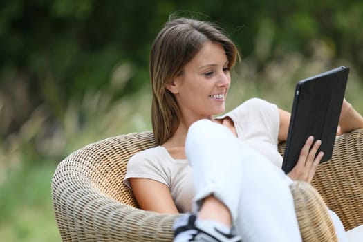 Woman relaxing in outdoor armchair and using digital tablet
