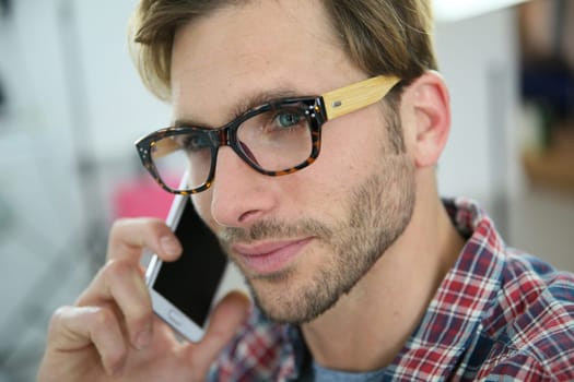 Trendy guy with eyeglasses talking on phone in office