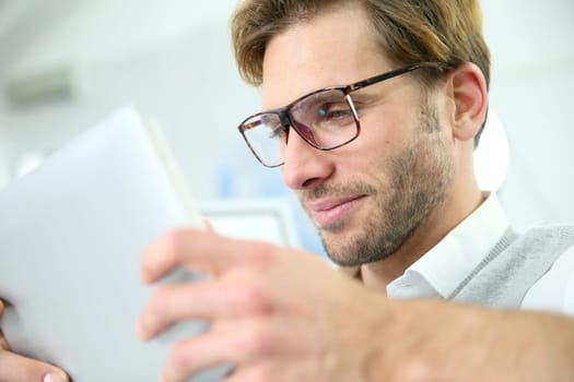 Man in office working on digital tablet, wearing eyeglasses