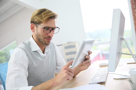 Man in office working on digital tablet, wearing eyeglasses