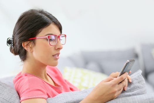 Brunette girl with red eyeglasses reading message on smartphone