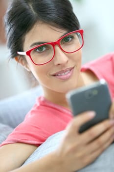 Brunette girl with red eyeglasses reading message on smartphone