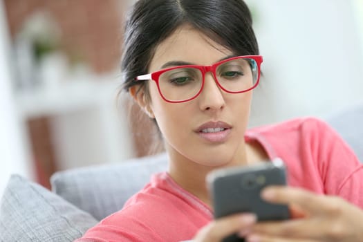 Brunette girl with red eyeglasses reading message on smartphone