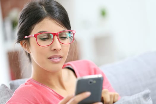 Brunette girl with red eyeglasses reading message on smartphone