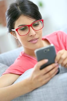 Brunette girl with red eyeglasses reading message on smartphone