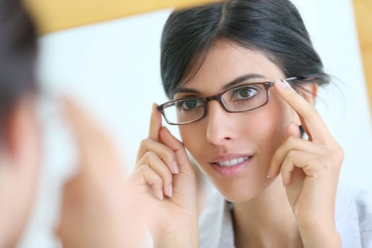 Portrait of young brunette woman trying eyeglasses on