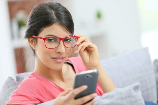 Brunette girl with red eyeglasses reading message on smartphone
