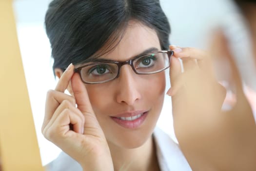 Portrait of young brunette woman trying eyeglasses on