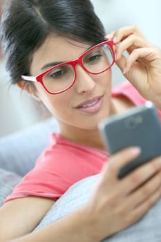 Brunette girl with red eyeglasses reading message on smartphone
