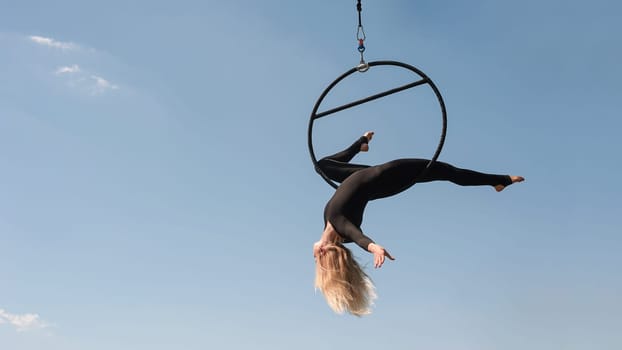 Sport woman doing exercises with a hoop, outdoor, against the blue sky. Sports equipment and lifestyle concept. Antigravity yoga.