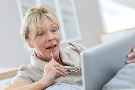 Senior woman with eyeglasses using digital tablet at home