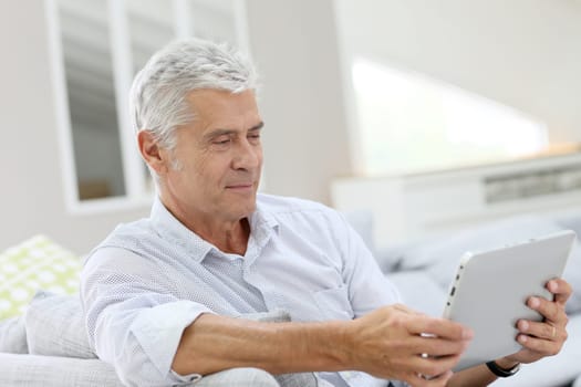 Senior man relaxing in sofa and using digital tablet