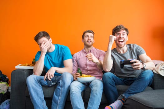 Group of three are having fun at home, playing video games.