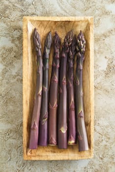 Fresh uncooked purple asparagus stalks in wooden bowl