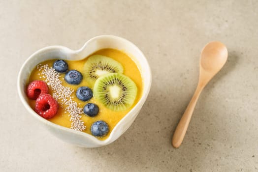 Peach smoothie bowl with blueberries, kiwi, white chia seeds and raspberries in a heart shaped bowl