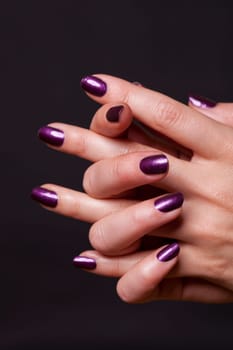 Female hands with purple fingernails as a close-up isolated against a black background