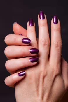 Female hands with purple fingernails as a close-up isolated against a black background