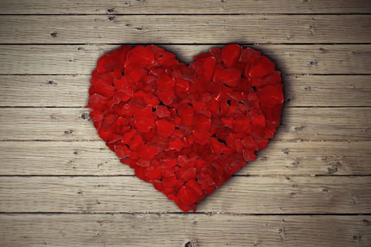 Rose petals arranged in shape of heart on wooden table.