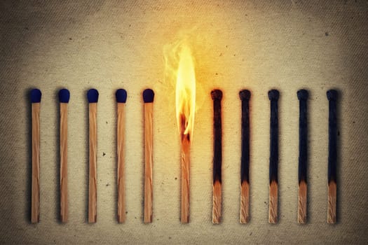 Burning match standing middle a row of whole, new matches at left and extinguished at right. Leadership concept