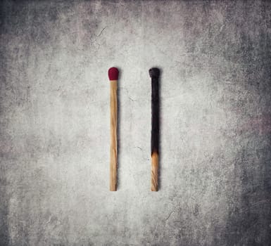 Close-up of a burnt match and a whole red match isolated on a gray background
