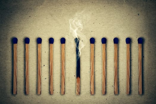 Extinguished, burnt match between a row of whole, new matches